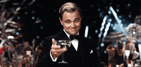 GIF of Leonardo DiCaprio raising a glass with fireworks behind him