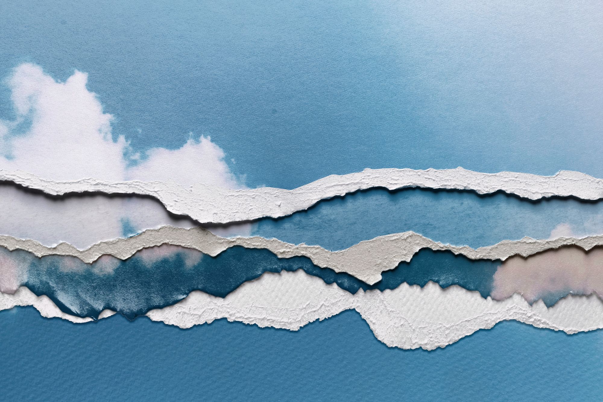 Torn pieces of paper depicting white clouds on a blue sky, one of top of the other.