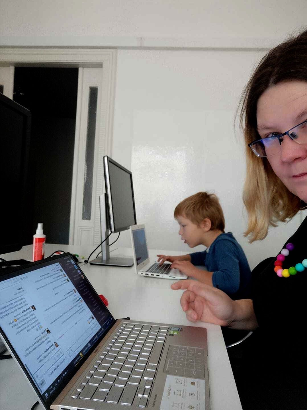 woman sitting behind a computer with her son next to her, also on a laptop