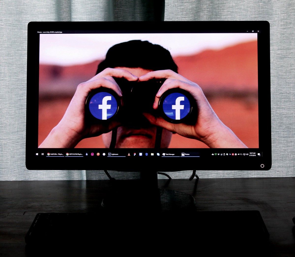 Computer desktop wallpaper of a person  with a binoculars reflecting the facebook logo.